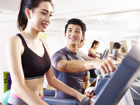 young asian adults exercising on treadmill helped by male trainer