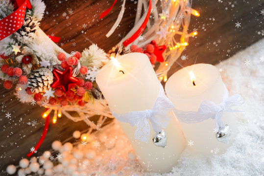 White candles on the snow with Christmas wreath and Christmas lights.