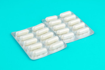 Packs of white capsules packed in blisters with copy space on turquoise background. Focus on foreground, soft bokeh. Pharmacy drugstore concept