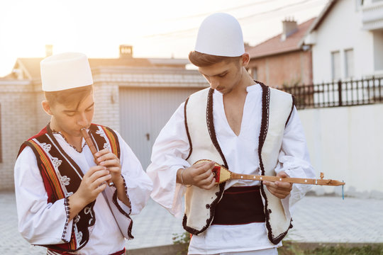 teen boys in traditional albanian costume playing music with flute and string instrument in the evening sunlight