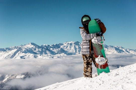 Snowboarder hugging the snowboard against the high mountain peaks