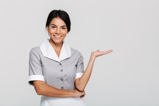 Close-up Portrait Of Young Happy Housekeeper In Uniform Showing Empty Palm While Looking At Camera