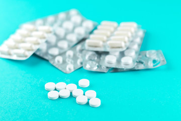 Full and empty packs of white capsules and pills packed in blisters with copy space on turquoise background. Focus on foreground, soft bokeh. Pharmacy drugstore concept