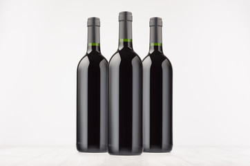 Three black wine bottles with red wine on white wooden board, mock up. Template for advertising, design, branding identity.