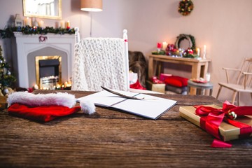 Wrapped gift, santa hat, diary and quill pen on wooden table in