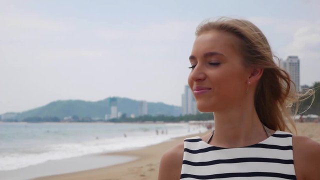 Young woman in black and white dresses walking alone on a tropical beach and looking at camera over background at storm on the sea. Travel Concept.