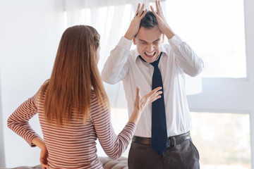 Emotional quarrel. Angry irritated emotional man standing in a light room and closing his head with...