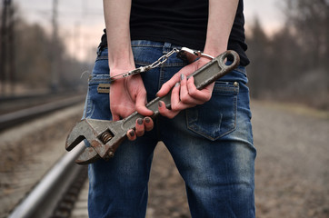The girl in handcuffs with the adjustable wrench on the railway track background. The concept of crime prevention with the participation of the railway and trains.