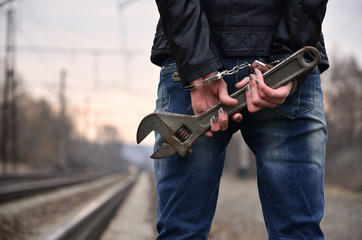 The girl in handcuffs with the adjustable wrench on the railway track background. The concept of crime prevention with the participation of the railway and trains.