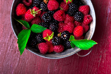 Blackberry and raspberry in a metal bowl on red wooden background. Top view.