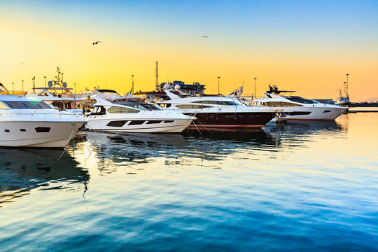 Fototapeta Luksusowe jachty zadokowane w porcie morskim o zachodzie słońca. Parking morski nowoczesnych łodzi motorowych i błękitnej wody. Podróże i modne wakacje.