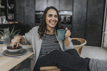 Glücklich lachende Frau sitzt mit Kaffee am Frühstückstisch