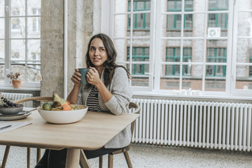 Junge Frau sitzt an Fr&uuml;hst&uuml;ckstisch mit Tasse