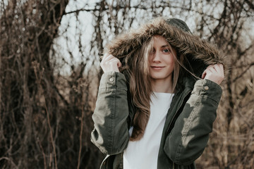 Beautiful young woman with blonde hair, wide eyebrows and blue eyes looking at camera. Girl posing at camera in green jacket. Blond girl in warm winter jacket with hood posing on camera. © darakaliton