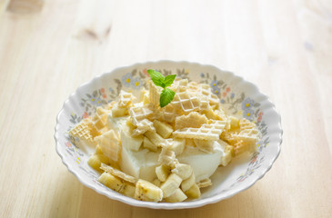 Vanilla ice cream in a plate with pieces of waffle and mint