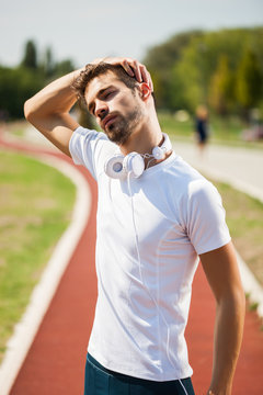 Young man is exercising on sunny day. He is stretching his body. 