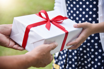 Asian woman giving a white gift box to elderly man.