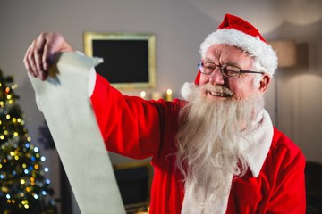 Naklejka premium Santa Claus reading scroll in living room