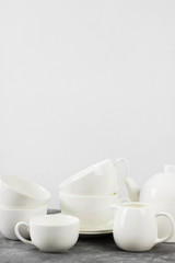 Clean white tableware (teapot, cups, saucers) on a gray background