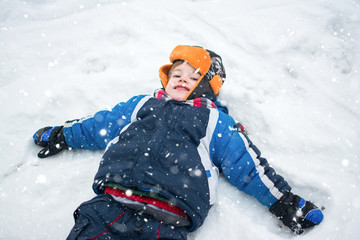 Fototapeta na wymiar Above view of little boy in winter clothes lying on snow and making a snow angel.