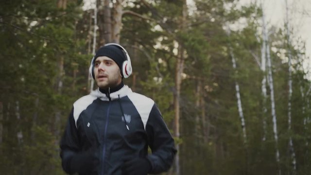 Handsome runner man in headphones jogging while listening music in winter park in the morning