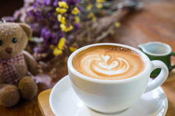 Hot latte art coffee in white cup with mini teddy and dry flower in the background