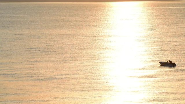 Pescatore sulla sua barca mentre pesca sul mare calmo e pieno ri riflessi