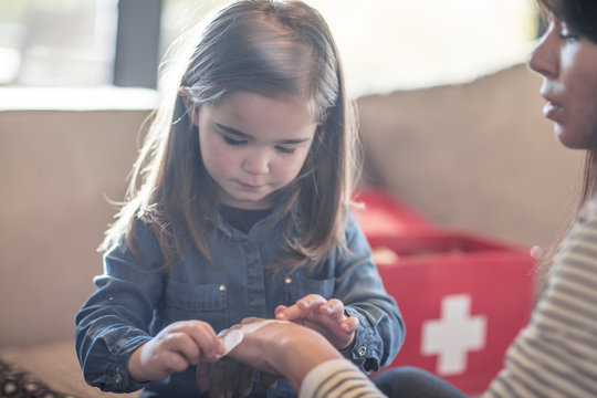 Girl sticking plaster onto mother's hand