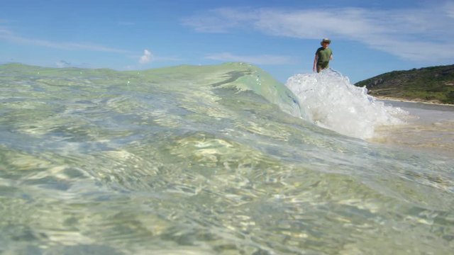 Shot in slow motion, a man in a green shirt walks calmly on the coast.