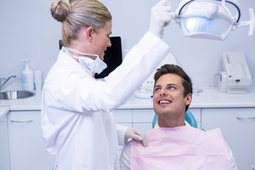 Dentist adjusting electric light while patient sitting on chair