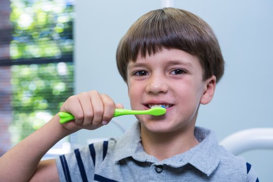 Boy holding toothbrush while sitting on chair at medical clinic