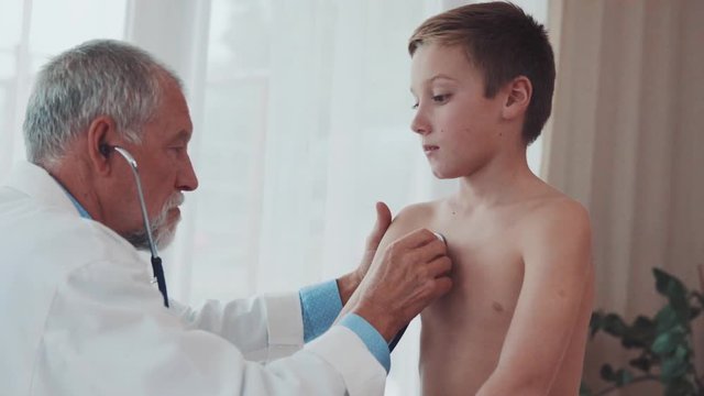 Senior doctor examining a small boy in his office.