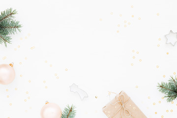 Minimal styled Christmas background with gift box, blush baubles, fir branches and baking molds on white. Holiday flat lay, top view.