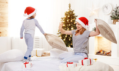 Fototapeta premium happy family mother and child daughter at christmas morning fighting pillows in bed