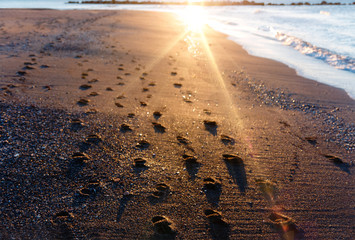 Footprints on a tropical beach with the sea lapping and golden sunrise shining through the sea water