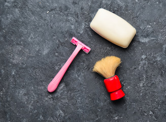 Accessories for simplified depimp. A razor, soap, a brush on a black concrete table.