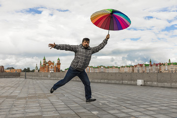 the bearded man on the embankment jumping like a child with colored umbrella in the hands
