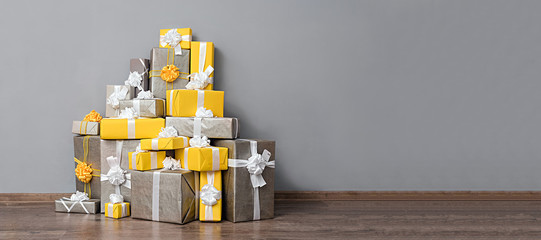 A pile of yellow and grey Christmas gifts with ribbons against the wall on a beautiful hardwood floor with copyspace