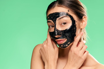 Beautiful young woman on a green background in a black coal face mask