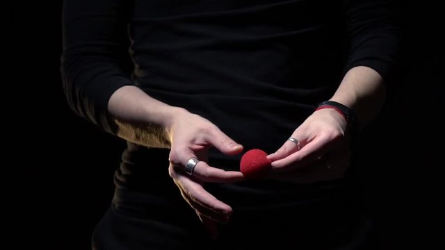 Magician in a black jacket shows a trick with a red ball