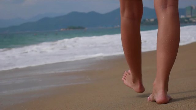 Woman bare foot walking on the summer beach. close up leg of young woman walking along wave of sea water and sand on the beach. Travel Concept.
