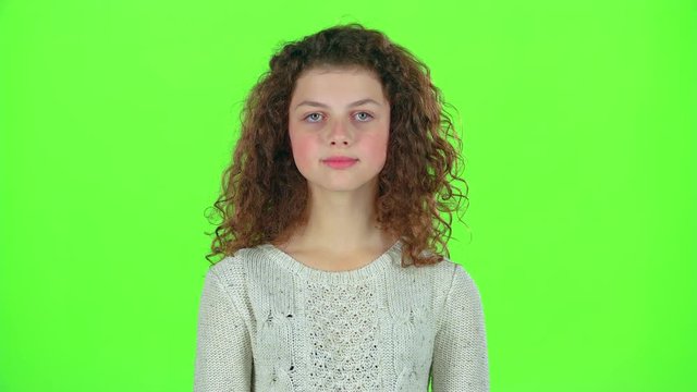Teenage girl smiles and looks into the distance, covering her face with her hands. Green screen
