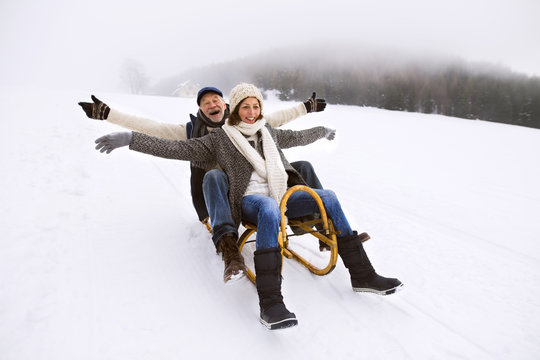 Senior couple having fun with sledge walking in the snow