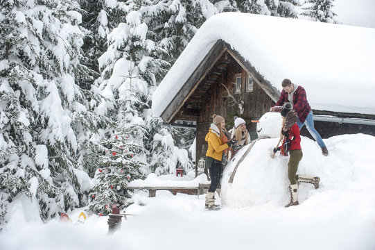 Austria, Altenmarkt-Zauchensee, friends building up big snowman at wooden house