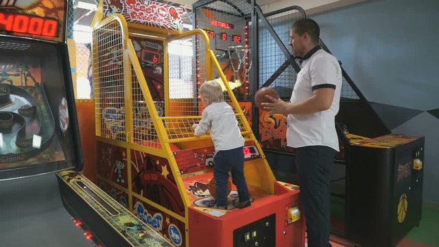 Family in gaming complex - small two-year-old boy with daddy throw the ball into the basket of colorful slot machine