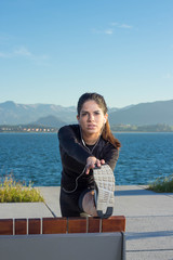 Fototapeta premium Young woman stretching on a bench with tha bay and mountains in the background. Front view.