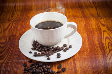 Hot coffee in white cup with coffee beans on wooden floor.