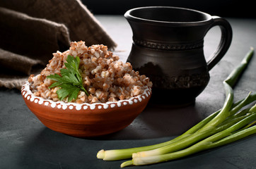 Buckwheat meal with cup of milk decorated with parsley and green onion on dark background