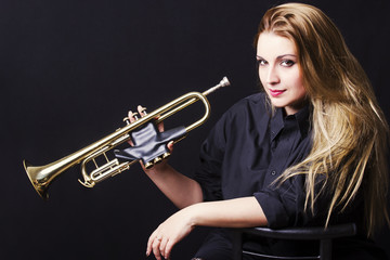 Portrait of young woman blowing on the trumpet isolated on black background