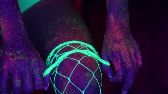 Closeup woman leg with fluorescent make up taking off fishnet stocking, creative makeup look great for nightclubs. Halloween party, shows and music concept - slow motion video